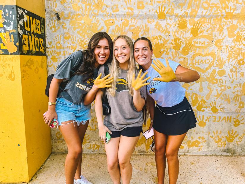 Three female students with gold hands at the painting of eagle walk event. 